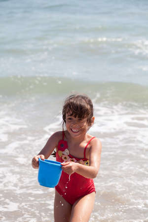 Very excited little girl running in the ocean surf with a blue bucketのeditorial素材