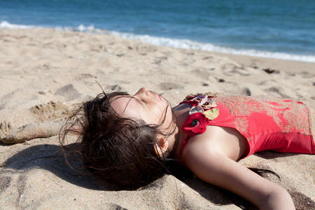 Little girl hanging out on the beach covered in sand. Closeup of a sleeping girl on the beach with ocean in the backgroundのeditorial素材