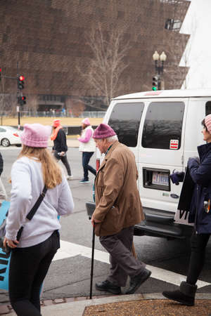 Older man with a walking cane donning a pink hat crossing Constitution Avenue with the new African American Museum in the background to reach the rally site to protest President Trump's positions on women's and other human rights. Credit: Dasha Rosato/Alaのeditorial素材