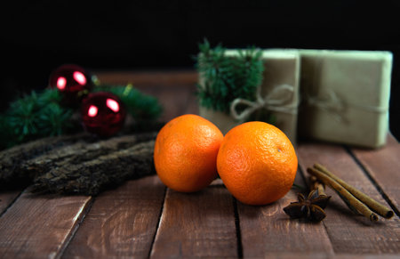 Tangerines lie on a brown wooden board on a black background, with wrapped gifts, Christmas tree...
