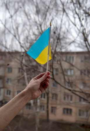 A standing man on a gray, holds in his hands background a yellow-blue cardboard Ukrainian flag with the inscription "Pray for Ukraine"の写真素材