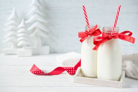 Festive bottles of milk with bows and straws on white wooden background with christmas trees decorationsの写真素材