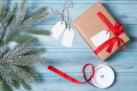 Gift wrapping, gift box with tags, ribbon and snow fir tree branch, wooden background, top viewの写真素材