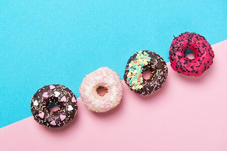 Assorted colored donuts in a row, minimalism on a blue and pink background, top viewの写真素材
