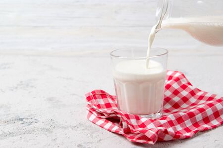 Pouring fresh milk from jug into a glass, light backgroundの写真素材
