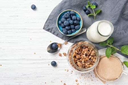 Granola muesli, milk and ripe blueberries with mint leaves, healthy breakfast concept, wooden background, top viewの写真素材