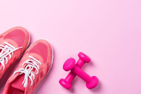 Fitness concept, pink sneakers and dumbbells on pink background, top view with copy spaceの写真素材