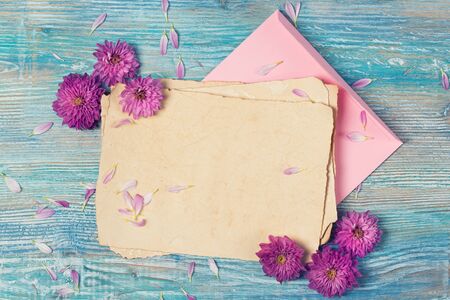 Old blank paper, envelope and pink flowers on blue wooden table, grunge vintage backgroundの写真素材