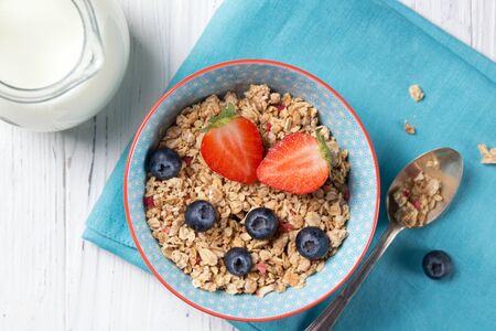 Healthy breakfast, bowl with granola muesli with strawberry and blueberry and milk jug, wooden background, top viewの写真素材