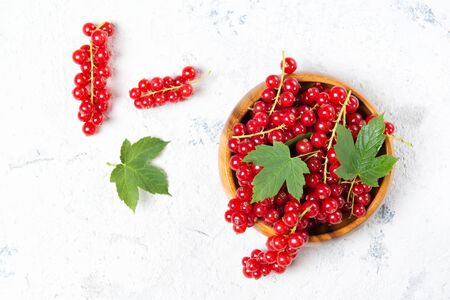 Ripe and juicy red currant with leaves in wooden bowl on stone table, top viewの写真素材
