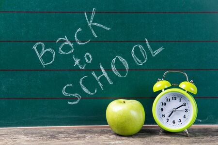 Alarm clock and apple on the green chalkboard with back to school text, education conceptの写真素材