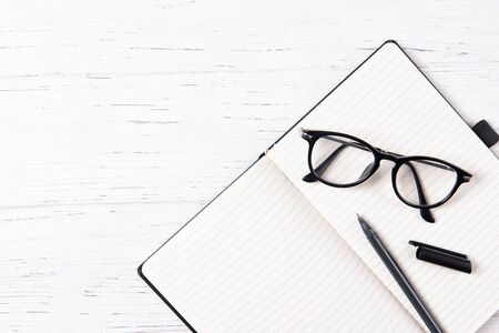 Office desk with empty notepad, pen and glasses, wooden background, top view with copy spaceの写真素材