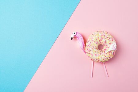 Fresh tasty donut in a shape of flamingo, on pink and blue background, top viewの写真素材
