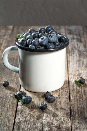 Fresh blueberries in enameled cup, rustic background, selective focusの写真素材