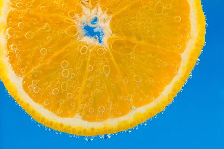 Slice of orange in the water with bubbles, on blue vibrant backgroundの写真素材