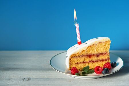 Slice of birthday cake with candle and berriesの写真素材