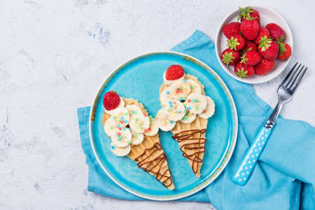 Sweet waffles with banana and strawberry in a shape of ice cream cone, meal for kids idea, top viewの写真素材