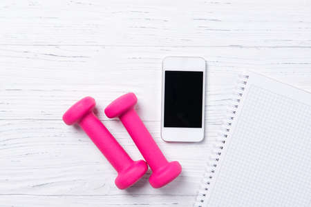 Fitness concept, pink dumbbells, smart phone and notebook on wooden background, top view with copy spaceの写真素材