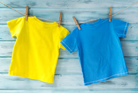 Two bright baby t-shirts hanging on a clothesline on a blue wooden backgroundの写真素材