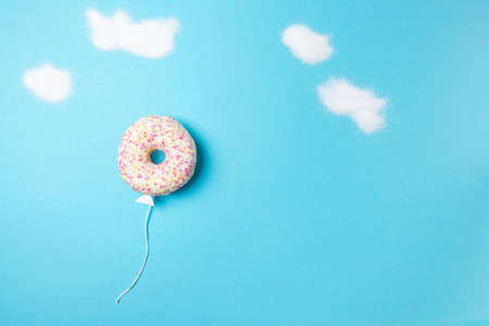 Donut on blue background, creative food minimalism, donut in a shape of balloon in the sky with clouds made of sugar, top viewの写真素材