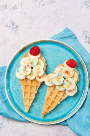 Sweet waffles with banana and strawberry in a shape of ice cream cone, meal for kids idea, top viewの写真素材