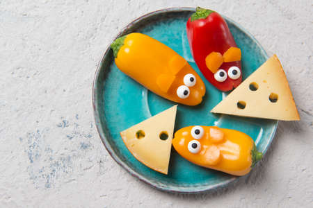 Colorful sweet mini peppers in the shape of mouses and pieces of cheese on a plate, stone table, top view, snack for kids ideaの写真素材