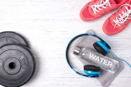Fitness concept, pink sneakers, bottle of water, weight plates and blue headphones on wooden background, top viewの写真素材