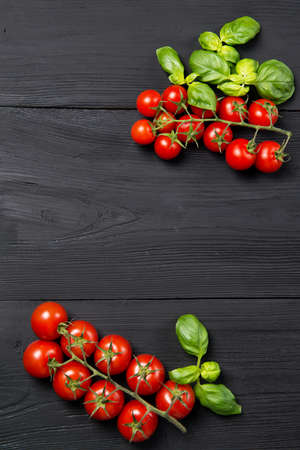 Ripe red cherry tomatoes in different size with fresh basil leaves on black wooden table, top view with copy spaceの写真素材