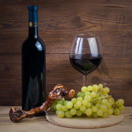Bottle and glass of red wine, grapes and corkscrew made of vine