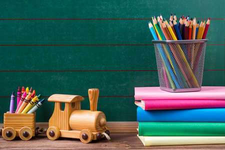 Back to school concept, colored pencils, wax crayons and books with toy train on empty chalkboard backgroundの写真素材