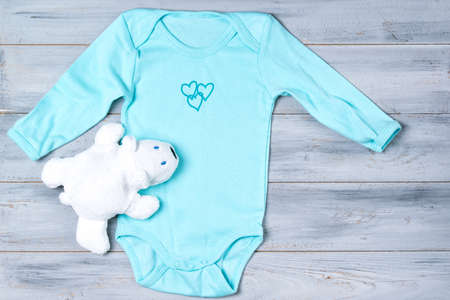 Baby clothes and white toy bear on a wooden backgroundの写真素材