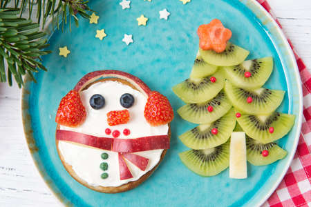 Christmas pancakes in a shape of snowman made of fresh fruits and berries and kiwi christmas tree. Glass of fresh milk. Healthy food for kids ideas. Top viewの写真素材