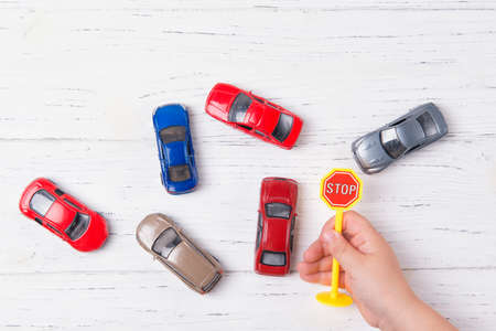 Child hands playing with miniature toy cars and stop sign, wooden background, top viewの写真素材