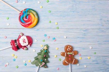 Sweet candies on a stick in shapes of Christmas tree, Gingerbread man and Santa Claus, Christmas card on a wooden backgroundの写真素材