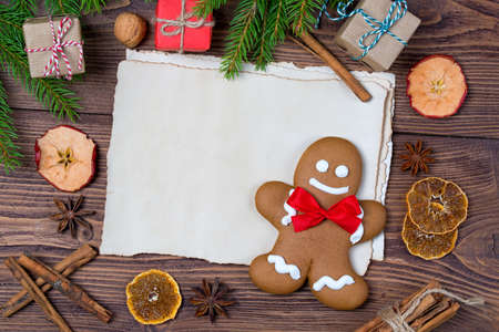 Christmas greeting card, old blank paper sheet, gingerbread man with frame made of fir, and spices, wooden backgroundの写真素材