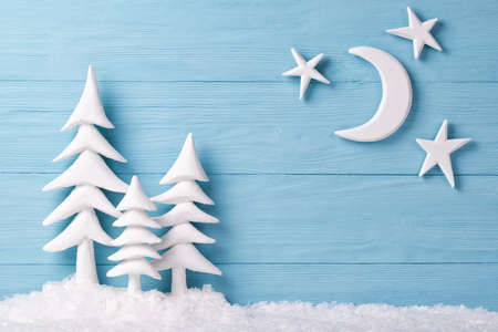 Christmas background with white christmas trees, snow, moon and stars, blue wooden backgroundの写真素材