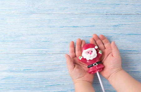 Candy in the shape of Santa in the child hands, Christmas concept on wooden backgroundの写真素材