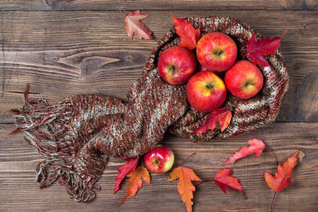 Apples in the scarf and autumn leaves, wooden background, top viewの写真素材