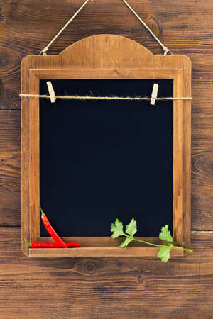 Aged blackboard with chilli peppers and parsley hanging on wooden wall, copy space for your menuの写真素材