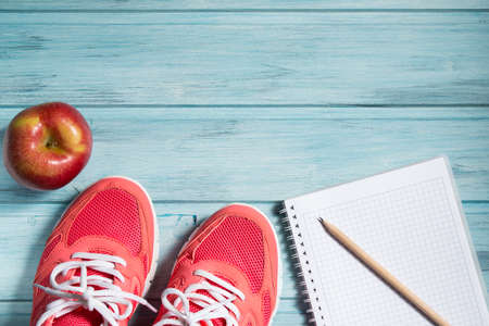 Fitness concept, pink sneakers, red apple and notebook with pencil on wooden background, top viewの写真素材