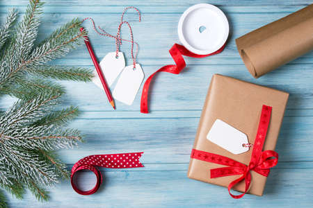 Gift wrapping, gift box with tags, ribbon, paper and snow fir tree branch, wooden background, top viewの写真素材