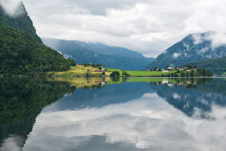 Landscape with lake and rural land with colored houses, mirror reflection of the mountains in the water, Norwayの写真素材