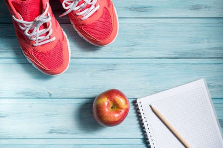 Fitness concept, pink sneakers, red apple and notebook with pencil on wooden background, top viewの写真素材