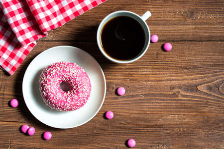 Pink donut on a plate with cup of coffee and pink candies, wooden background, top viewの写真素材