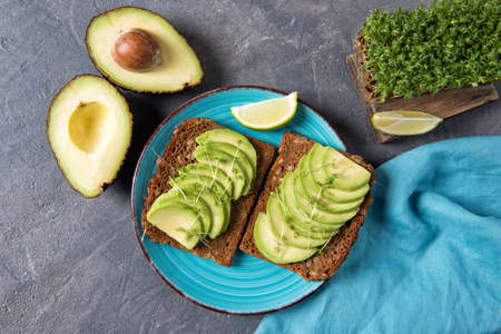 Avocado toasts on whole grain bread, sliced avocado with garden cress sprouts and lime, healthy eating concept, top viewの写真素材