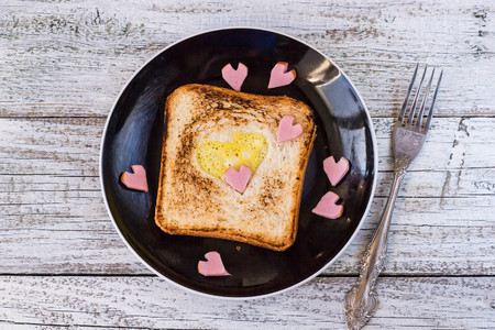 breakfast for the celebration of Valentine's day - toast with scrambled eggs in the form of hearts, sausages in a plate and a forkの写真素材