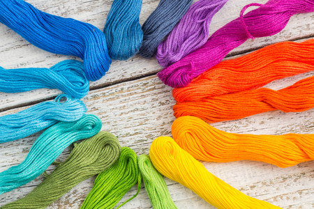 colorful sewing threads for embroidery on white wooden background