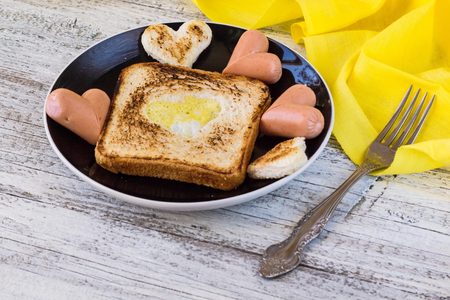 breakfast for the celebration of Valentine's day - toast with scrambled eggs in the form of hearts, sausages in a plate and a forkの写真素材