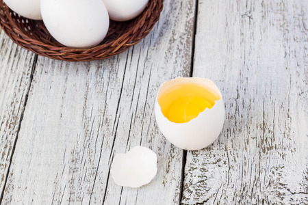 Broke One whole egg amongst white eggs in basket on a white wooden backgroundの写真素材