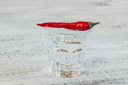 Shot of vodka with cayenne pepper on an old white wooden tableの写真素材